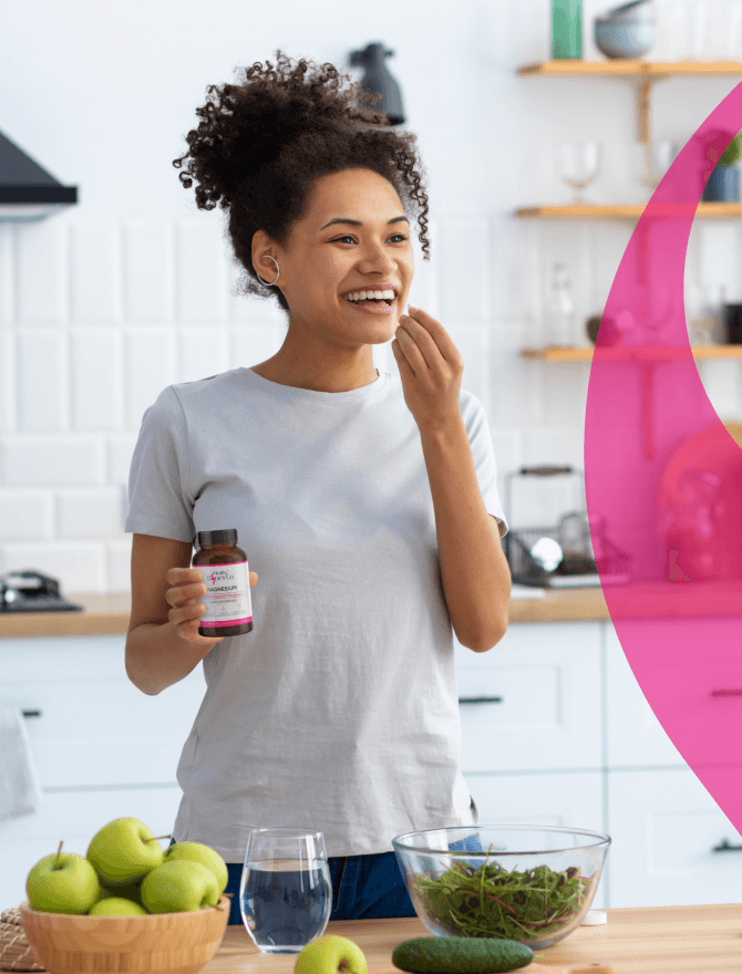 A woman in a kitchen surrounded by fresh green vegetables and fruits, holding a Healthy Bones Co. product in one hand.