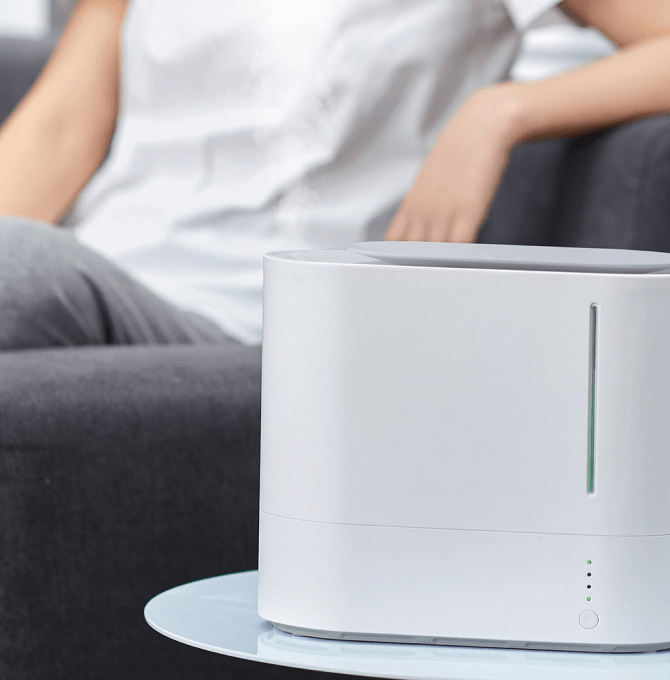 An air purifier on a table near a woman sitting on a couch.