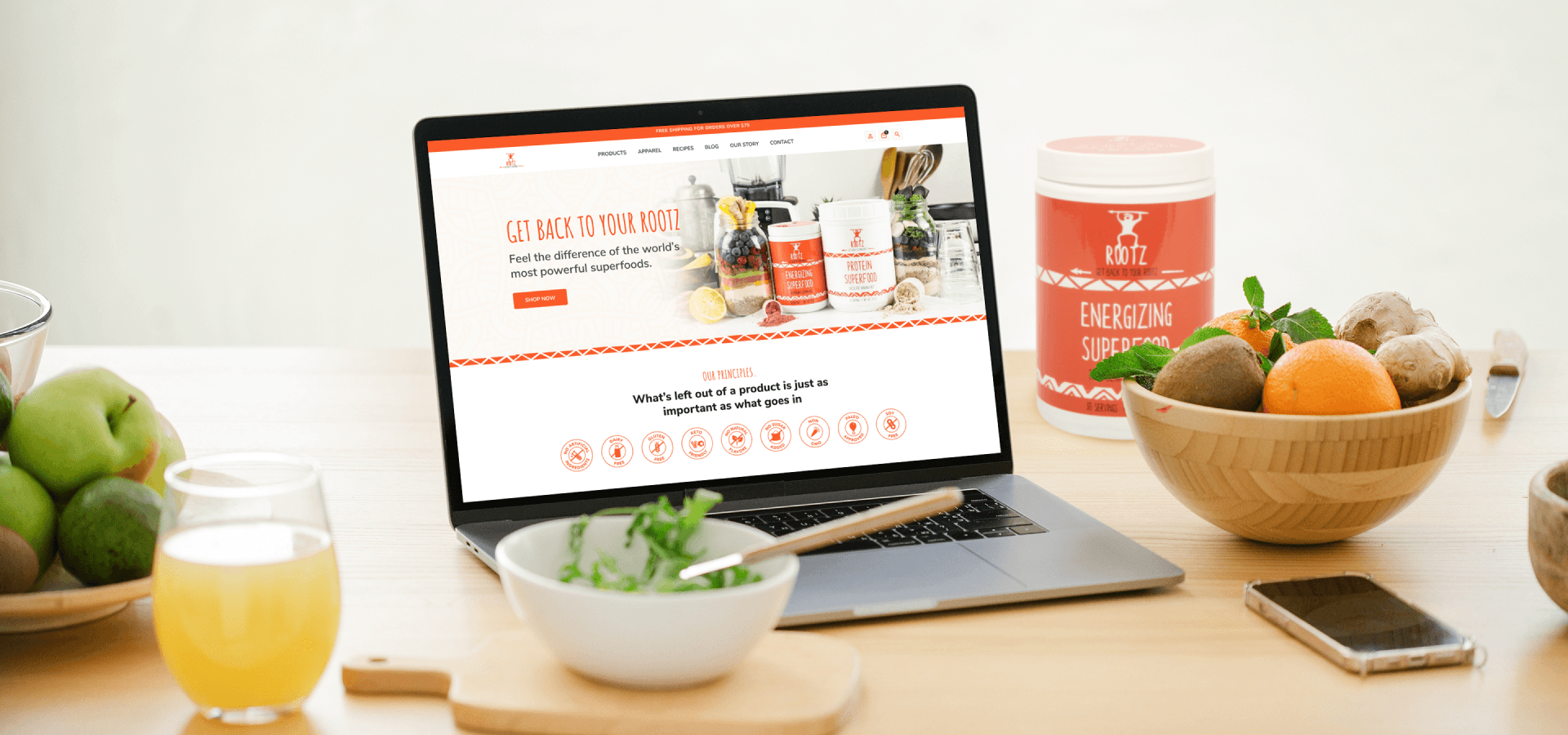 A laptop showing Rootz website on a table with food and the Energizing Superfood canister.